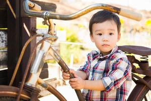 menino caucasiano e chinês de raça mista se divertindo na bicicleta. foto