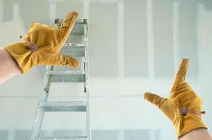 empreiteiro mãos em luvas de couro emoldurando novo drywall em branco foto