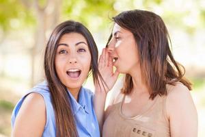 duas lindas irmãs gêmeas étnicas sussurrando segredos ao ar livre. foto