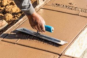 trabalhador da construção civil usando espátula em cimento molhado formando coping ao redor da nova piscina foto