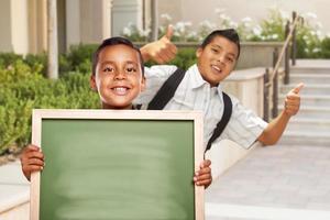 meninos com polegares para cima segurando quadro de giz em branco no campus foto