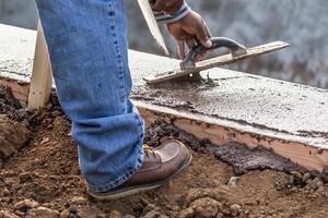 trabalhador da construção civil usando espátula de madeira em cimento úmido formando coping ao redor da nova piscina foto