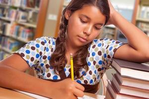 aluna hispânica com lápis e livros estudando na biblioteca foto