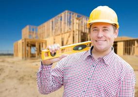 empreiteiro masculino sorridente no capacete segurando plantas e nível no canteiro de obras em casa. foto