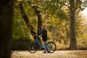 jovem com bicicleta elétrica no parque de outono foto