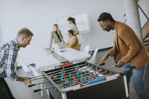 jovens empresários multiétnicos casuais jogando futebol de mesa e relaxando no escritório foto