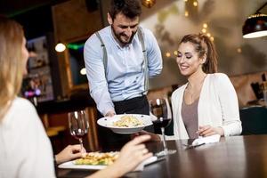 jovem garçom servindo comida para clientes do sexo feminino no restaurante foto