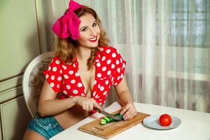 linda jovem alegre pepino fatiado na cozinha e sorrindo para a câmera foto