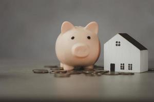 finanças, casa de madeira com um cofrinho rosa e muitas moedas de dinheiro. economize dinheiro e conceito imobiliário. foto