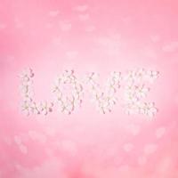 palavra amor disposta de flores de macieira branca em pano de fundo rosa com bokeh em forma de coração. vista superior, configuração plana. foto