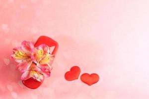 flores alstroemeria em vaso vermelho e dois corações têxteis vermelhos em fundo de bokeh de corações rosa. plano de fundo do dia dos namorados. foto