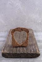 uma fatia de pão de centeio com buraco esculpido em forma de coração na velha placa de madeira no pano de fundo de concreto cinza. foto