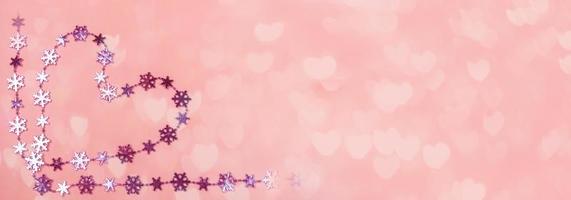 banner criativo do dia dos namorados. coração de flocos de neve lilás brilhantes sobre fundo rosa suave com bokeh em forma de coração. foto
