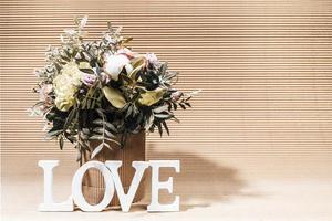 arranjo ecológico com buquê de flores em vaso diy e letras brancas amor em caixa bege com espaço de cópia. foto