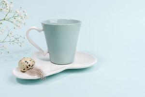 composição mínima de páscoa para café da manhã de férias com lindo par de chá, ovo de codorna, flores brancas em azul claro. foto