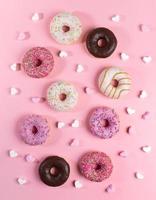 composição criativa de donuts com esmalte multicolorido e pequenos marshmallows em forma de coração no pano de fundo rosa da moda. foto