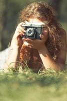 menina bonita hippie na grama tirando fotos com uma câmera velha - foto de efeito vintage