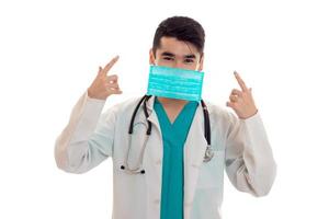 médico masculino de uniforme e máscara com estetoscópio posando isolado no fundo branco foto