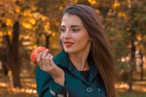 linda garota com batom vermelho olha para sorrisos e mantém a maçã na mão foto