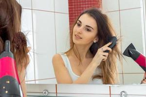 linda garota seca o cabelo na frente de um espelho
