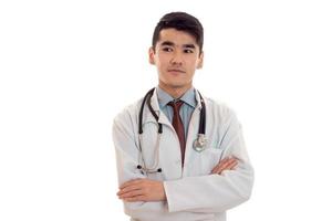 retrato de um jovem médico moreno de uniforme com estetoscópio posando e olhando de lado isolado no fundo branco foto