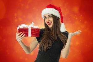 menina sorrindo com chapéu de Papai Noel com presente vermelho foto