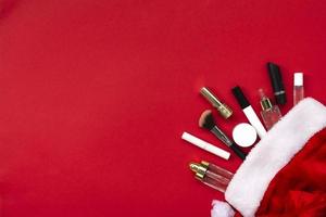composição plana leiga com produtos de maquiagem e decoração de natal em fundo de papel vermelho. natal, feliz ano novo 2021, conceito de desejos femininos. foto