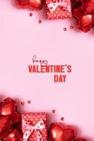 feliz dia dos namorados cartão formato vertical com caixa de presente, velas e balões de forma de coração vermelho em fundo rosa foto