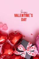 feliz dia dos namorados texto e caixa de presente, velas e balões de forma de coração vermelho no fundo rosa. cartão de dia dos namorados formato vertical foto