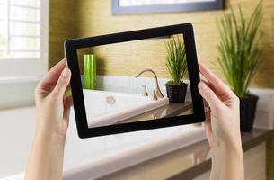 mãos femininas segurando um tablet de computador no banheiro com foto na tela.