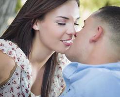 casal romântico de raça mista se beijando no parque foto