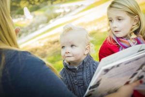 mãe lendo um livro para seus dois filhos loiros adoráveis foto