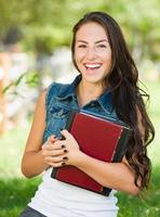 estudante atraente e sorridente de raça mista com livros escolares ao ar livre foto