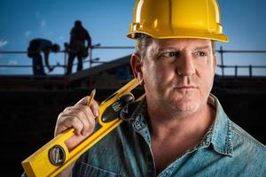 empreiteiro sério no capacete segurando nível e lápis no canteiro de obras. foto