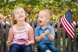 jovem irmã e irmão comparando o tamanho da bandeira americana no banco do parque foto