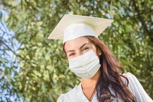 pós-graduação feminina em boné e vestido usando máscara facial médica foto