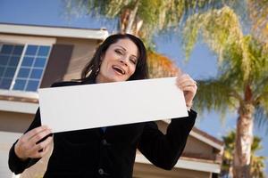 atraente mulher hispânica segurando placa em branco na frente de casa foto