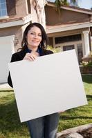 atraente mulher hispânica segurando placa em branco na frente de casa foto