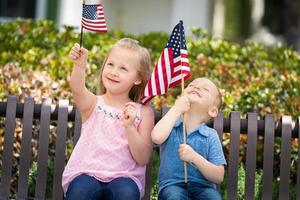 jovem irmã e irmão comparando o tamanho da bandeira americana no banco do parque foto