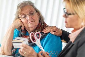 consultor financeiro entregando tesouras para senhora sênior segurando cartões de crédito foto