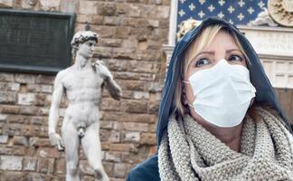 jovem usando máscara facial caminha perto da estátua de davi na piazza della signoria itália foto