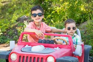 jovens irmãos chineses e caucasianos de raça mista usando óculos escuros brincando no carro de brinquedo foto