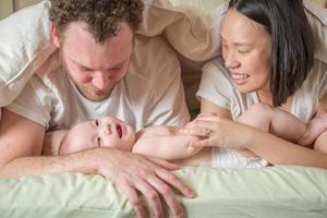 menino chinês e caucasiano de raça mista deitado na cama com seus pais foto
