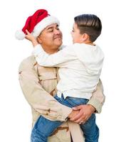 soldado masculino hispânico usando gorro de Papai Noel segurando filho mestiço isolado em um fundo branco foto