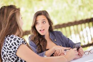 namoradas jovens adultas expressivas usando seu telefone celular inteligente ao ar livre foto