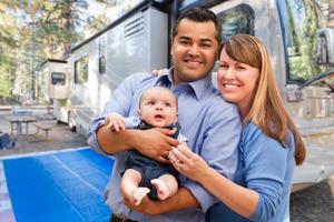 feliz casal multiétnico caucasiano e hispânico com bebê na frente de seu lindo trailer no acampamento. foto