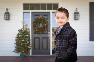 menino jovem de raça mista na varanda da frente da casa com decorações de natal foto