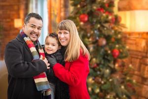 retrato de família jovem de raça mista na frente da árvore de natal dentro de casa. foto