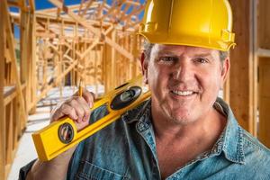 empreiteiro sorridente no capacete segurando nível e lápis no canteiro de obras. foto