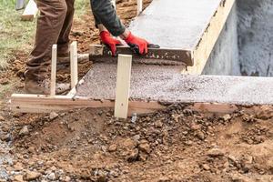 trabalhador da construção civil nivelando cimento molhado em moldura de madeira foto